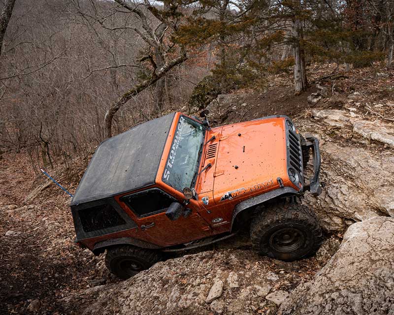 Orange jeep diving up rock hill