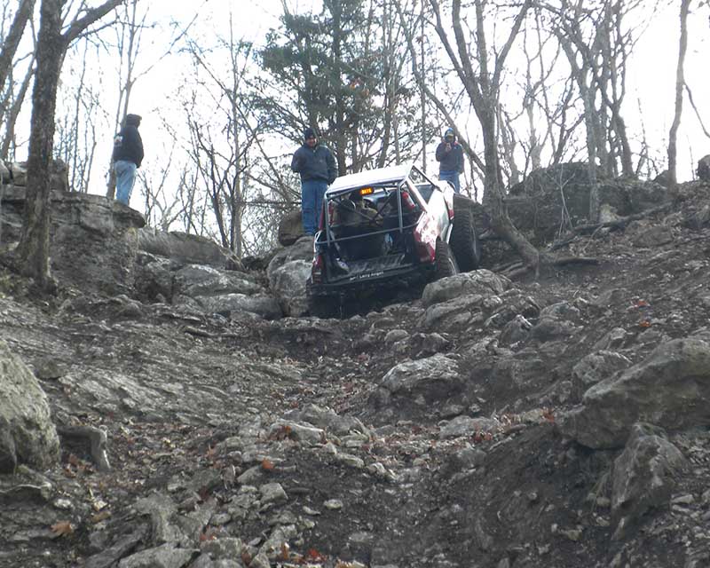Off road truck climbing up rock hill with people standing at the top